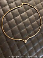 Full view of the 14 inch sterling silver choker necklace laying flat on black quilted surface showing the smooth silver chain and front zirconia stone.