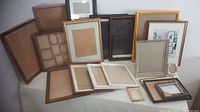 Photo of overall assortment of picture frames arranged on table. Shows variety of frame sizes and styles including gold, brown, black, pink and white frames. Some frames have multi-photo mats and show signs of wear.