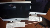 Two Apple iMac computers side by side with keyboards and mice on a wooden surface