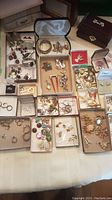 Wide view of assorted costume jewellery grouped in boxes of various sizes and a large wooden box, arranged on a flat surface.