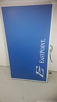 Blue EastPoint branded ping pong table surface, folded and standing upright against a wall.