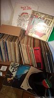 Wide view of vinyl records collection in boxes and stacks with visible album covers including Rock 'n' Roll High School and Iggy Pop & James Williamson.