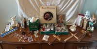 Wide shot showing entire lot on table: prints, statues, boxed Belleek cherub, rosaries, crosses, medals, night lights, and candles.