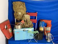 Photo showing the full collection of camping gear including cooler, backpacks, pots, pan, folding chair, stool, lantern, and life jackets.