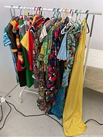 Photo showing a rack of 14 colorful vintage polyester clothing items including dresses, shirts, and skirts with varied prints and patterns
