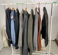 Nine jackets and sweaters hanging on white rack showing variety of leather, wool, and knit materials and colors