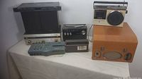 Photo showing the complete lot of vintage electronics on a table including the orange Clarke and Smith reel to reel tape recorder, Koyo radio, GE cassette recorder, Eico amplifier with Wharfedale speakers, and Fostex multitracker.