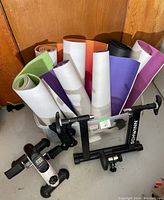 Yoga mats rolled in assorted colors and a Schwinn bicycle trainer shown with clamp mechanisms