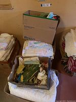 Boxes of assorted folded bed linens, towels, and assorted fabrics in various colors and patterns.