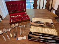 Full view of all items on table: Rogers Stainless cutlery set in wood box, two Sheffield carving sets in original boxes with antler handles, multiple serving utensils.