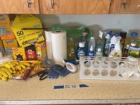 Photo showing assorted cleaning products, garbage bags, gloves, dusters, cleaning cloths, and brushes spread out on a counter