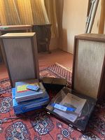 Photo showing vintage wooden speakers, Coby DVD player with remote on top of DVDs, and turntable base on rug.