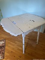 Farmhouse-style table with drop leaf sides extended, showing scalloped edges and distressed white paint.