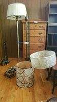 Full view showing one complete floor lamp with pleated lampshade, two disassembled lamp poles, and three vintage lampshades on the floor.