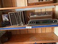 Philips 701 stereo with turntable, two speakers, Realistic cassette recorder, and boxed Vtech corded telephone on wooden shelves.