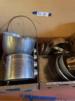 Two boxes filled with various metal cookware items including pots, pans, and bowls