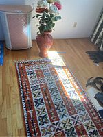 Rug, tall pottery vase, and plastic roses displayed on wooden floor showing overall set