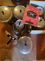 Set of Wear-Ever aluminum pots and pans, with lids and original Wear-Ever recipe booklet on top.