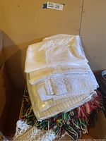 Stacked white fabric sheets with floral lace detailing and colorful Afghan throws underneath