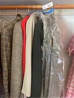 Five men's jackets and suits hanging on wooden hangers on a closet rod, some plastic-covered.
