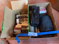 Photo showing a cardboard box with assorted cassette tapes, VHS tapes, and two black carrying cases filled with tapes