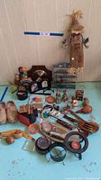 Photo shows a variety of vintage collectibles arranged on a blue surface against a wall, including wooden Dutch clogs, a straw scarecrow doll, a small metal spice rack, assorted small ceramic figurines, wooden and ceramic small decorative items, and utensils. Items show vintage wear.