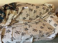 Full view of beige floral coverlet with diamond textured background and fringe, draped over a piece of furniture.