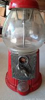 Front view of the red gumball machine showing glass globe and metal coin mechanism with a penny inserted.