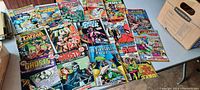 Top-down view of 15 vintage comics laid flat on table exhibiting cover artwork, various superhero and supernatural themes.