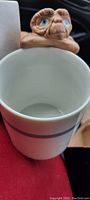 White porcelain coffee cup with a detailed figural handle of E.T. with blue eyes, shown inside the cup.