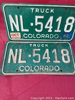 Pair of green metal Colorado truck license plates, number NL-5418, details of embossed white lettering and 1983 oct registration stickers