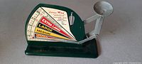 Side view of antique Jiffy-Way metal egg scale showing colorful size rating scale and weighing arm with round pan.