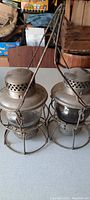Pair of vintage railroad lanterns side by side, steel frames and clear glass globes, hanging handles visible.