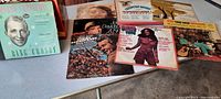 Photo of several vintage LP record album covers on a table including Bing Crosby, John Denver, and others showing condition and variety.
