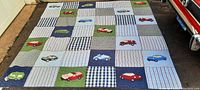 Full view of the colorful quilted bedspread with patchwork squares featuring sewn car designs, showing overall condition and size.