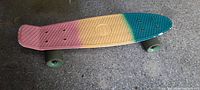 Tri-color vintage kids skateboard angled view showing pink to yellow to teal pattern on the deck with wide light green wheels.