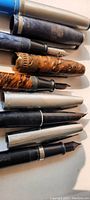 Close up of 8 vintage ink pens with caps, showing variety of colors and materials including marbled brown, silver and black.