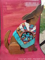 Front view of the wooden dog/wolf sculpture seated on a red chair, showing the southwestern bandana with colorful motifs tied around its neck.
