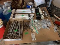 Overview of cabinetry accessories including metal brackets, various handles, knobs, railings, and mounting hardware in boxes on a table.