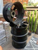 Four stacked black alloy car rims viewed from side showing inner surface and mounting holes.