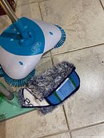 Blue and white Bissell spin broom with rotating brushes and detached microfiber mop pads on tiled floor