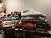 Stack of assorted comforters, throws, quilts, and bedspreads showing variety of colors and textures