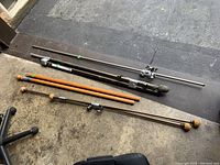 Photo showing five curtain rods lying on the ground including one wooden rod and four metal rods with various finials and clamps, taken from above.