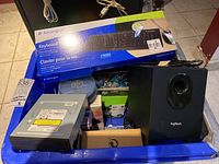 Overview of entire lot showing various electronics including Kensington keyboard in box, stacked Blu-ray discs, Logitech speaker, and various boxed items.
