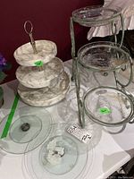 3-tier white faux marble lazy Susan serving tray with metal handle on left, 3-tier glass plant/candle holder with metal frame on right, and three separate glass lazy Susan rotating bases on table