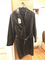 Black Danier leather coat hanging on a hanger, front view, showing smooth texture, three-button closure and belt detail.