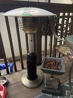 Photo of taller traditional patio propane heater with cylindrical black propane tank, metallic stem, protective grill, and reflector top.