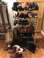 Front view of metal shoe rack with assorted shoes, boots, running shoes, and slippers organized on shelves and floor.