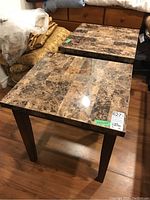 Pair of side tables showing marble-pattern laminate tops and dark wood veneer legs and bases on hardwood floor.