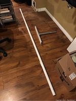 Full view of the long white support pole alongside its detached base on a wooden floor.